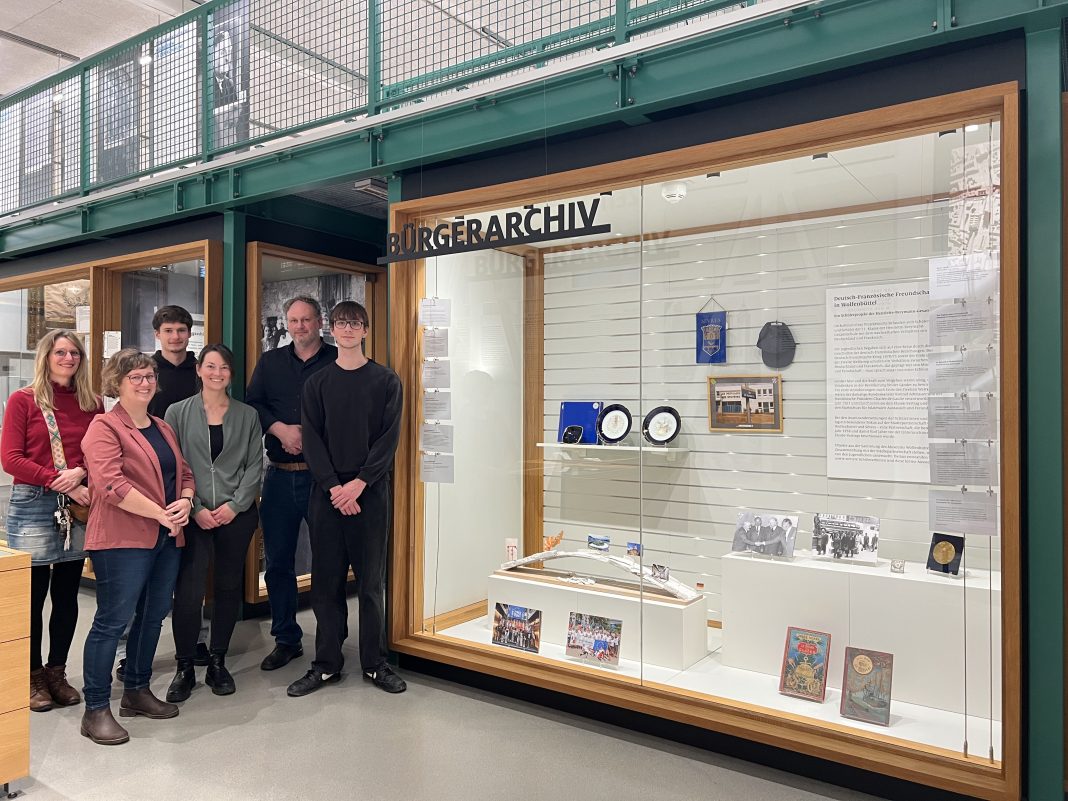 Sabrina Benner, Frauke Janzen, Stella Gilfert, Markus Gröchtemeier und die Schüler Elias Bormann und Kristers Millers bei der Vitrine